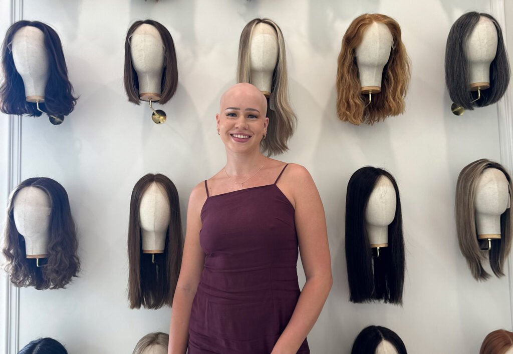 Woman with hair loss standing in front of human hair wig display in Toronto wig boutique